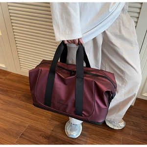Burgundy travel bag with sturdy black handles shown held in a modern living room