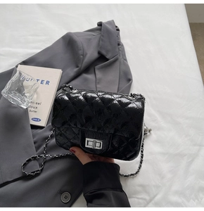 Gros plan du sac matelassé noir avec fermoir rotatif argenté sur fond de costume gris
