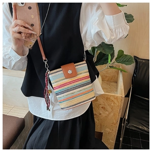 Détail du sac seau tissé coloré avec rabat en cuir marron et décoration à pompon