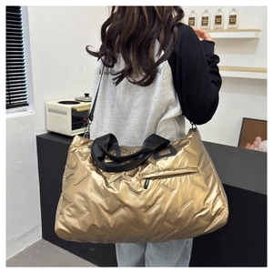 Macro detail of metallic gold quilted duffel bag featuring black nylon straps and zipper