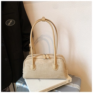 Minimalist beige suede baguette bag with long handles and double zipper detail on books