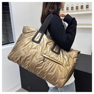 Detail of a large gold quilted tote bag featuring metallic finish and black strap