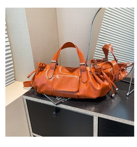 Detail of orange pebble leather baguette bag featuring buckle straps and side drawstring