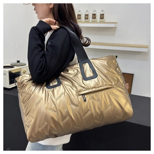 Detail of quilted metallic gold travel bag featuring black wide shoulder strap and pocket