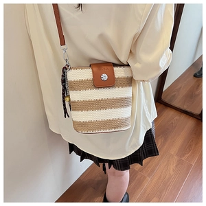 Détail du sac seau en tricot rayé avec rabat en cuir et pompon porté sur l'épaule
