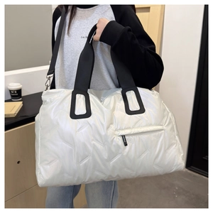 White quilted travel bag with glossy finish and black straps worn by a model in a shop