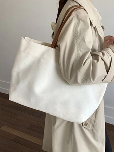 Minimalist off-white canvas tote bag with brown leather handles in a chic interior setting