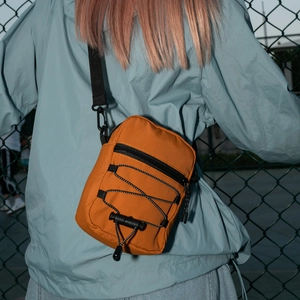 Outdoor shot showing the back view of a ginger nylon crossbody bag with drawstrings