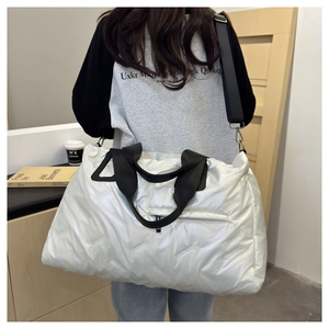 Silver quilted duffel bag with black straps worn by model for short travel or fitness
