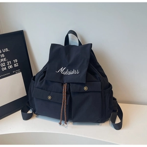 Detail view of the black nylon backpack showing flap embroidery and dual buckled front pockets
