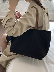 Minimalist black canvas tote bag with brown leather straps shown in a lifestyle view