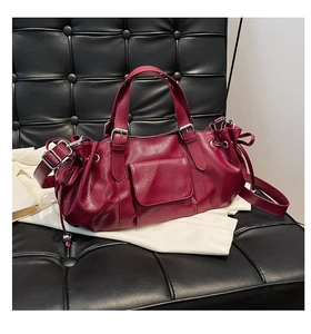 Close-up of wine red pleated leather shoulder bag with adjustable straps on sofa