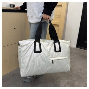 Detail of quilted white travel tote bag with high-gloss finish and black strap handles