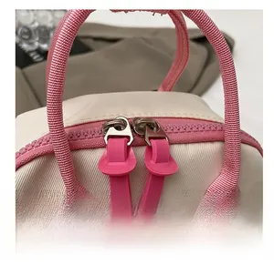 Detail of pink dual-way smooth zippers and nylon webbing handle on beige crossbody bag