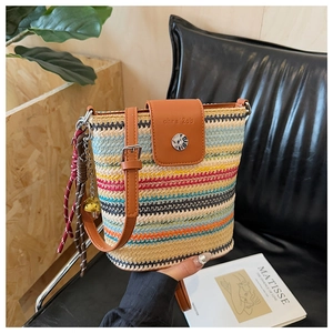 Détail d'un sac seau en paille colorée avec rabat en cuir marron et pompon élégant