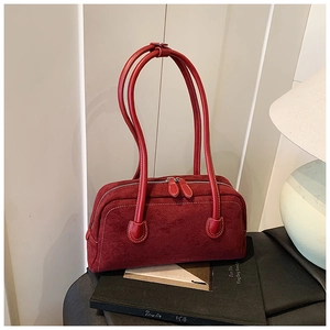 Close-up of a deep red baguette bag with white stitching and round handles on a black book