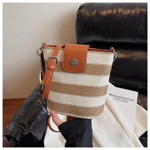 Détail d'un sac seau en paille tressée avec rabat en cuir marron et fermoir métallique