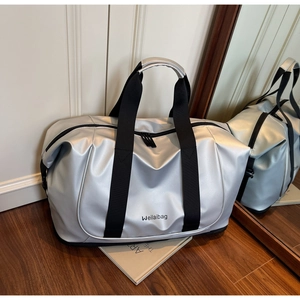 Silver metallic travel duffel bag with black handles on a wooden floor next to a magazine