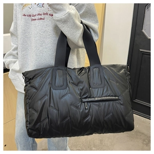 Detail of black quilted nylon tote bag featuring a front hidden zipper pocket and soft texture