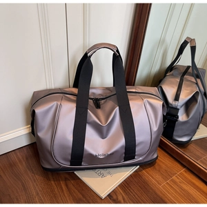 Close-up of champagne grey metallic travel bag with black nylon handles on a wood floor