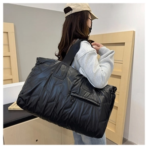 Quilted oversized travel tote bag in black glossy fabric worn by a model for size comparison