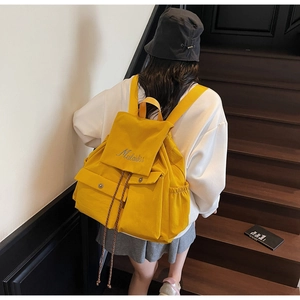 Detail of yellow canvas backpack with embroidery and drawstring closure on stairs