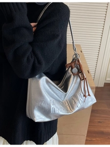 Silver metallic hobo shoulder bag with embossed letters and a woven leather charm