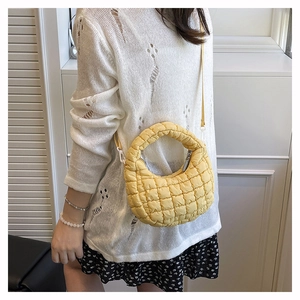 Detail of yellow quilted crossbody bag shown with adjustable strap and top handle