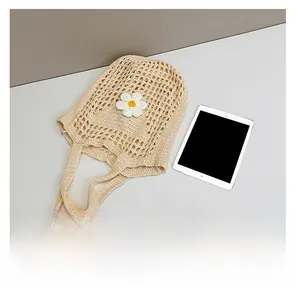 Détail du sac cabas en maille beige avec marguerite à côté d'une tablette pour la taille