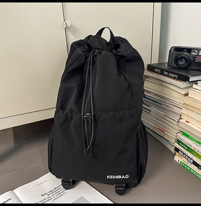 Close-up of black nylon drawstring backpack with KEMIBAG logo among books and camera