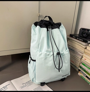 Detail of light blue nylon drawstring backpack with black accents and front pocket