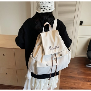 Detailed back view of a beige canvas backpack with embroidery and metal buckles on a model