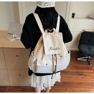 Detailed back view of a beige canvas backpack with hand-written embroidery and side pocket
