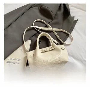 Dettaglio borsa a secchiello beige con trama litchi, fiocco e tracolla regolabile