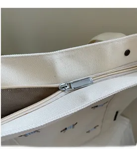 Détail de la fermeture éclair en métal et de la broderie de chien sur le cabas en toile