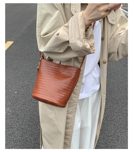 Detail of a brown woven leather bucket bag with a tight diagonal texture and strap