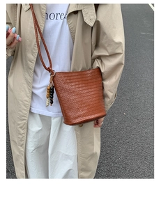 Detail of woven brown bucket bag featuring a beaded tassel charm and slim strap