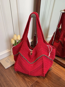 Red knit tote bag with green wavy trim and drawstring closure on a wooden floor