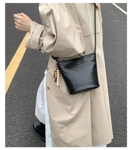Fashionable black woven bucket bag with wooden bead charm styled on a trench coat
