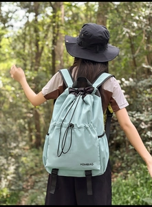 Outdoor shot showing back view of light blue nylon backpack with drawstring in forest