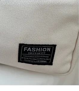 Close-up of off-white canvas tote bag with black woven label and detailed stitching