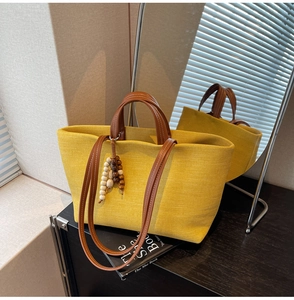 Close-up of yellow canvas tote bag with brown leather handles and wooden bead charm accessory