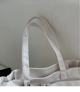 Detail of off-white canvas tote bag featuring reinforced stitching and dual handles