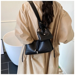 Detail of black pebbled leather crossbody bag with silver hardware on a trench coat