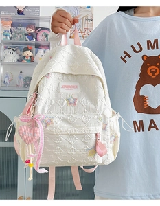 Detailed view of white quilted backpack with colorful star embroidery and heart charm