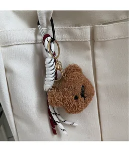Brown plush bear keychain charm with colorful woven strap on a white canvas tote bag