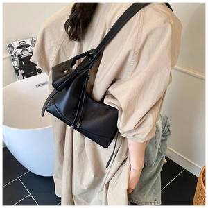 Detail of black lychee grain leather crossbody bag with drawstring side and matching strap