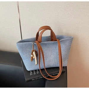 Detail of light blue denim tote bag with brown leather handles and wooden bead pendant