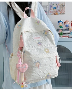 Close-up of white quilted backpack featuring colorful glitter stars and pink heart charm