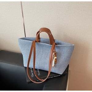 Detail of light blue canvas tote bag featuring brown leather handles and wooden bead charm
